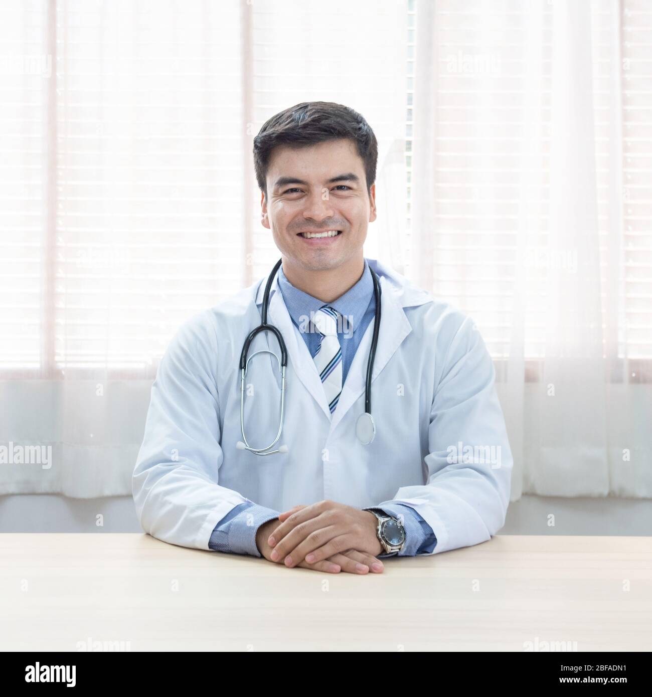 Joven doctor caucásico hombre sentado en el escritorio de su lugar de trabajo y sonriendo