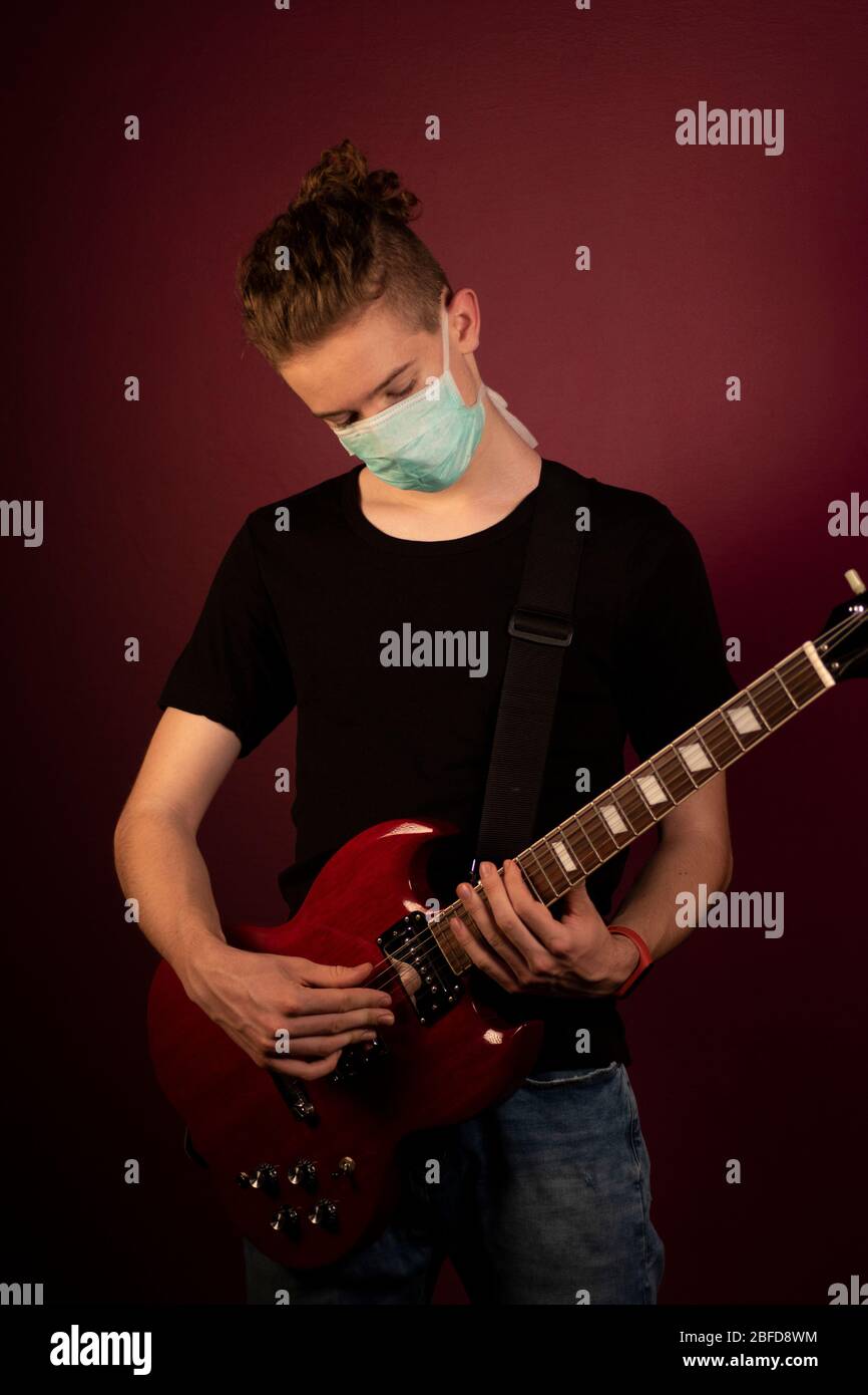 Coronavirus, cuarentena en casa, tocar la guitarra en máscara de protección Foto de stock