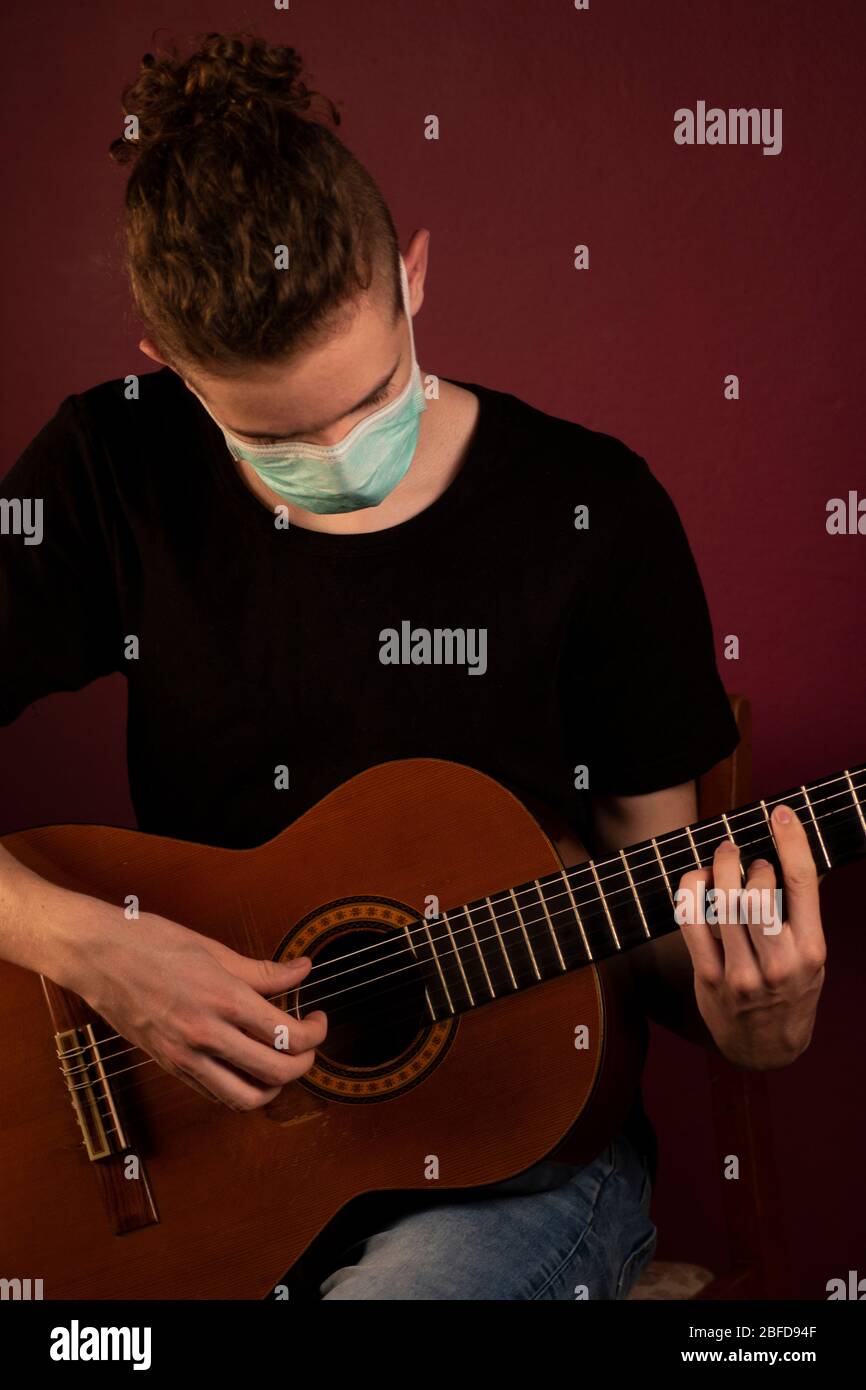 Coronavirus, cuarentena en casa, tocar la guitarra en máscara de protección Foto de stock
