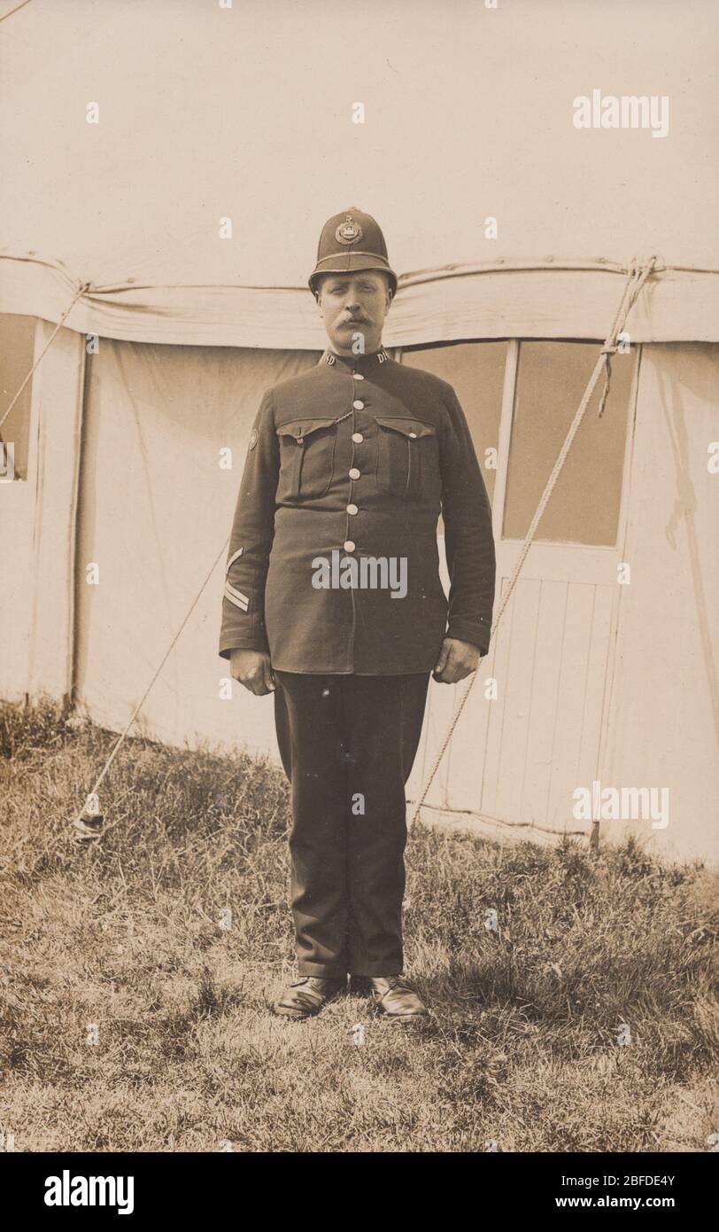 Vintage a principios del siglo 20 Posteta fotográfica que muestra un policía británico posando fuera de una tienda. Collar no D14. Foto de stock