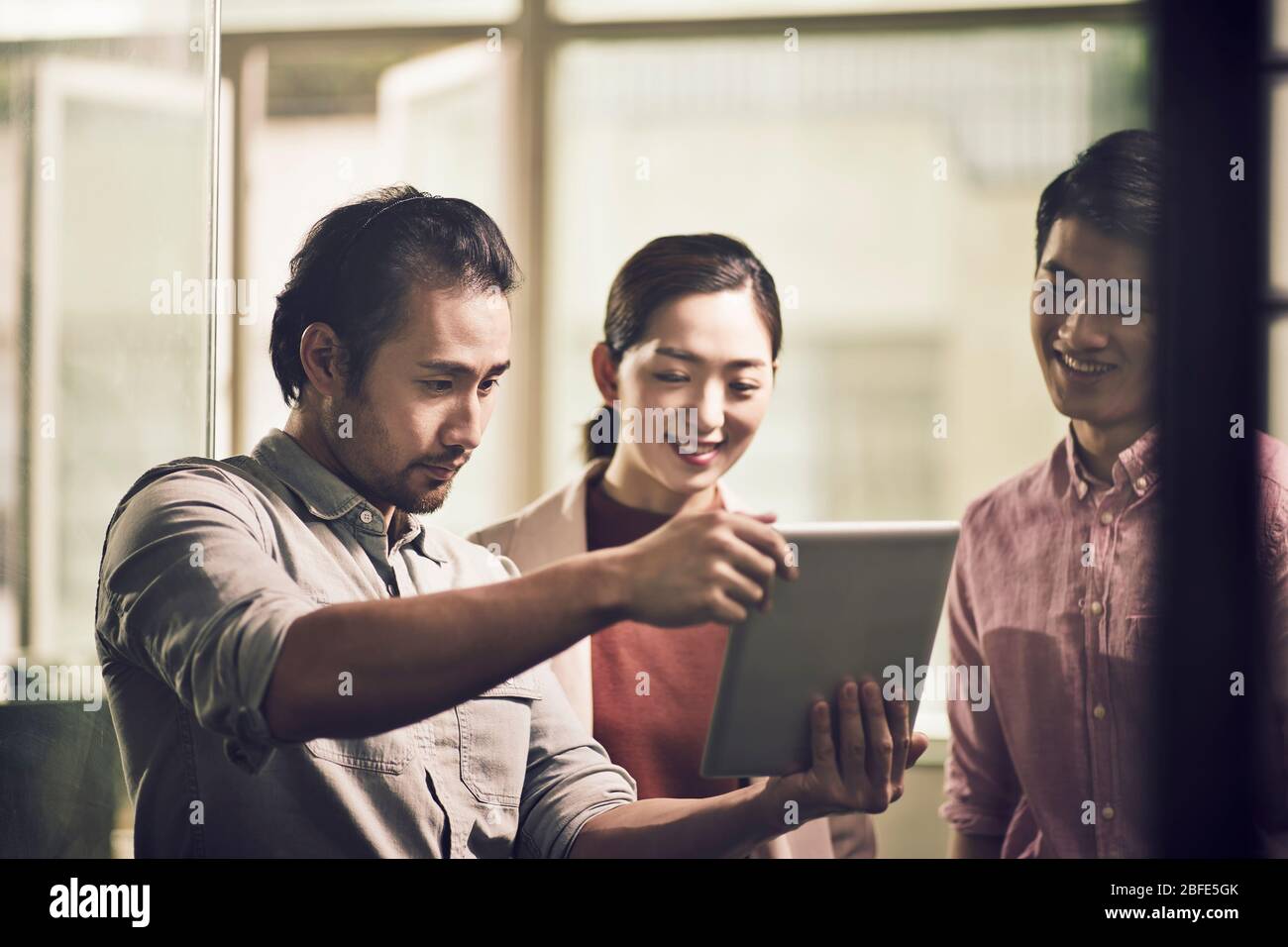 tres jóvenes empresarios asiáticos trabajando juntos en la oficina mirando la tableta digital Foto de stock
