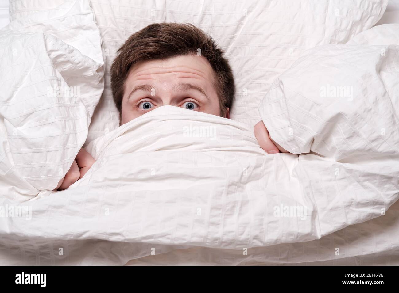 El hombre se despertó de una pesadilla, se cubrió la boca y la nariz con una manta y se ve asustado. Concepto de insomnio. Foto de stock