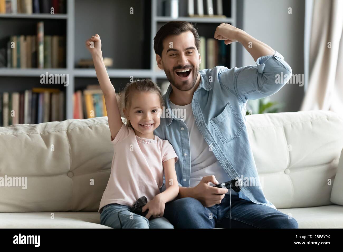 Padre su hija pequeña sostiene joystick jugando playstation celebrar el éxito Foto de stock