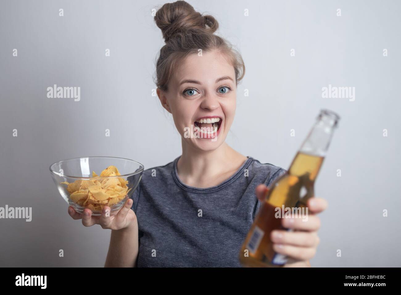 Sonriente joven mujer caucásica niña bebiendo una botella de cerveza y sosteniendo patatas fritas crujientes Foto de stock