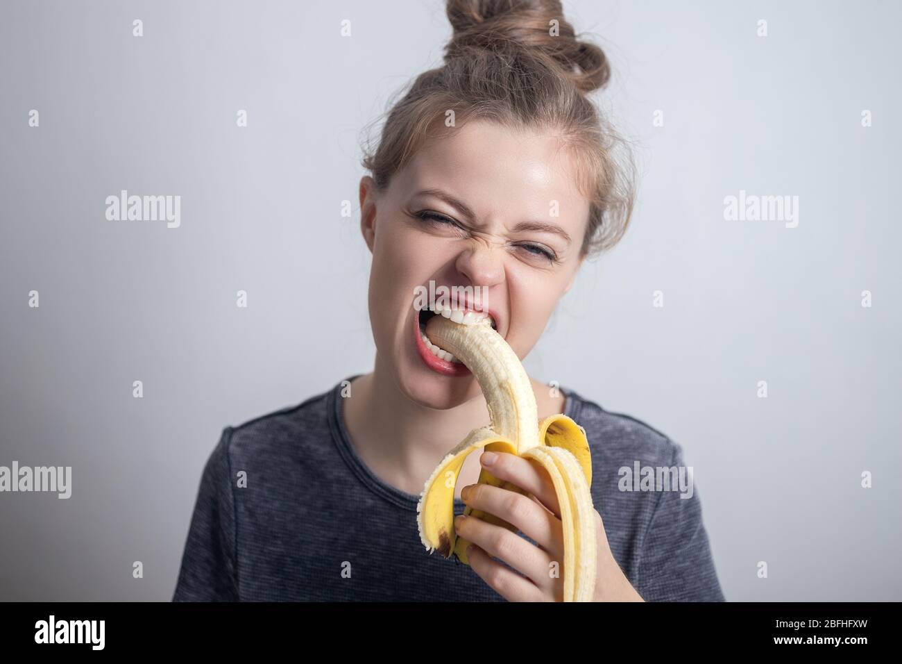 Joven mujer caucásica niña mordiendo plátano con cara divertida. Estilo de vida saludable, dieta vegetariana de frutas. Foto de stock