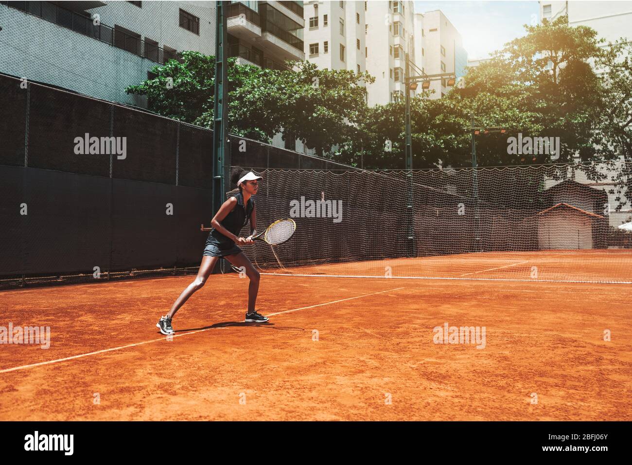 Una joven afroamericana delgada juega al tenis al aire libre en la pista de entrenamiento; hermosa biracial deportes chica en la posición deportiva listo para desviar diez Foto de stock