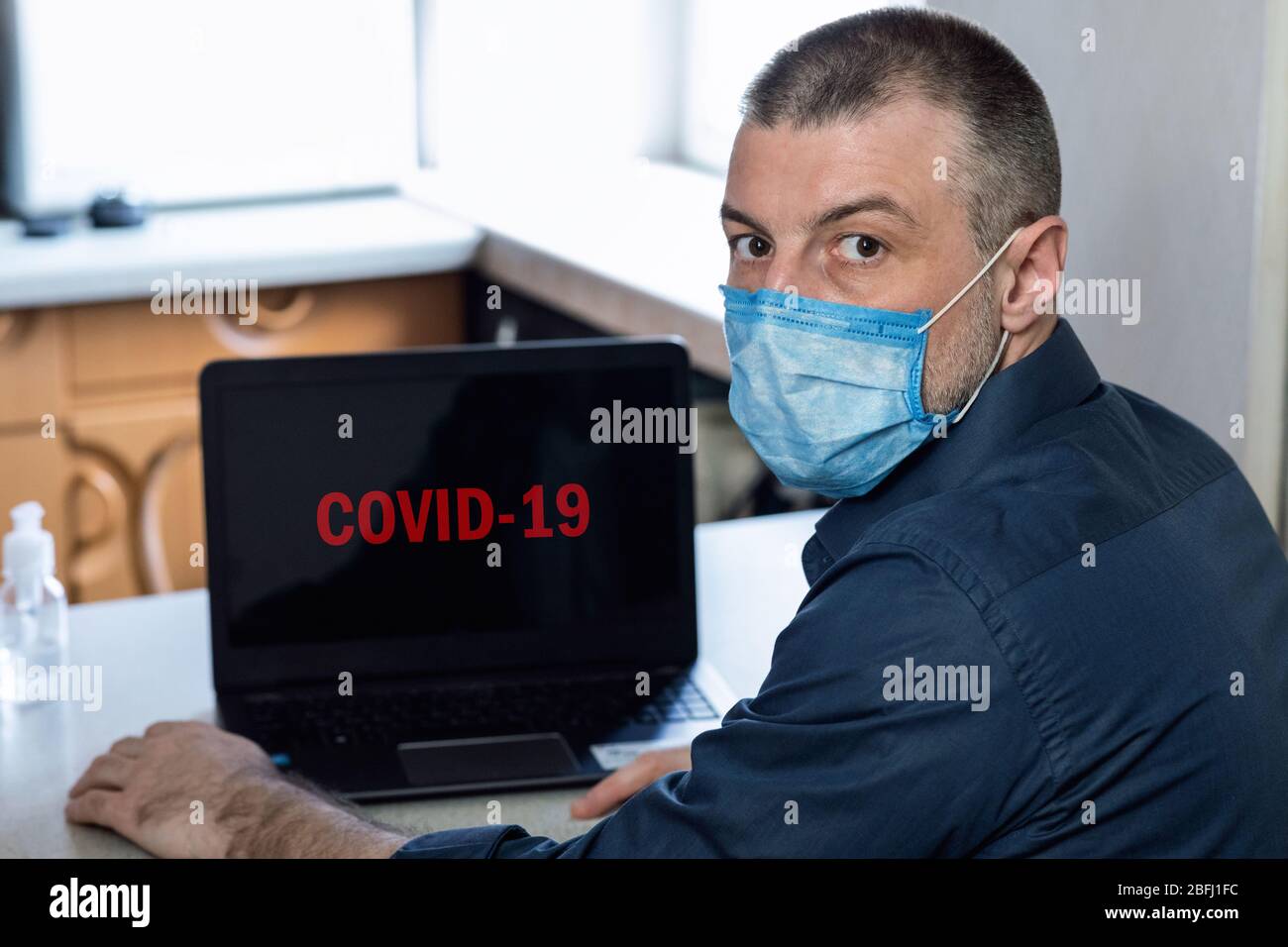 Hombre sentado en el portátil con COVID-19 en la pantalla interior Fotografía de stock - Alamy