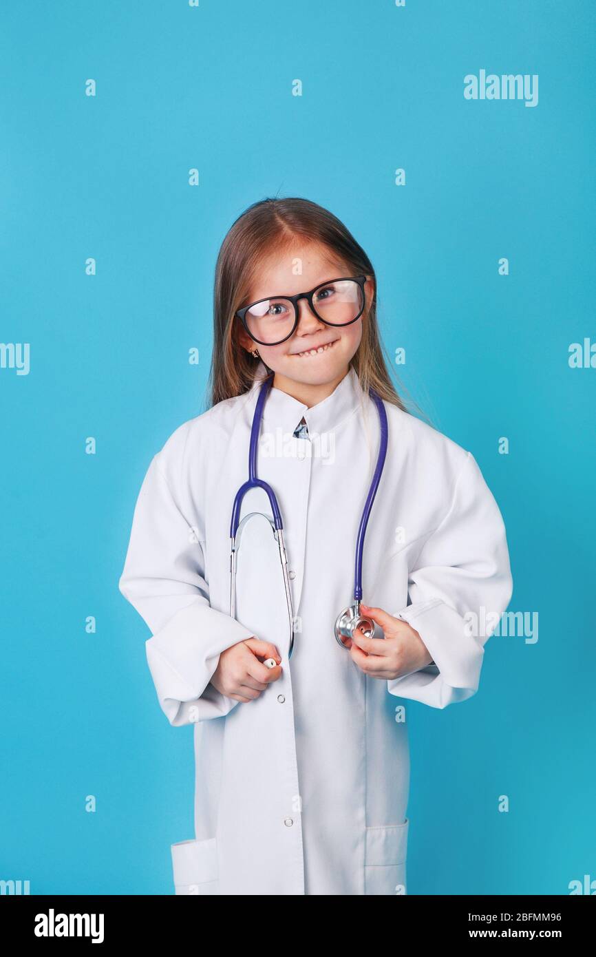 Niño lindo en abrigo del doctor y gafas con estetoscopio sobre fondo azul. Foto de stock