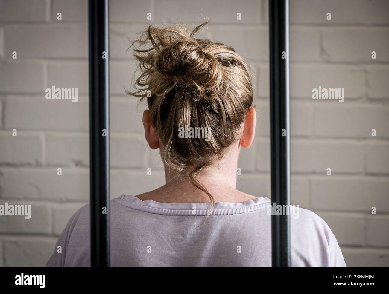 Una prisionera femenina detrás de las rejas en una prisión de mujeres. Imagen planteada por el modelo. Foto de stock