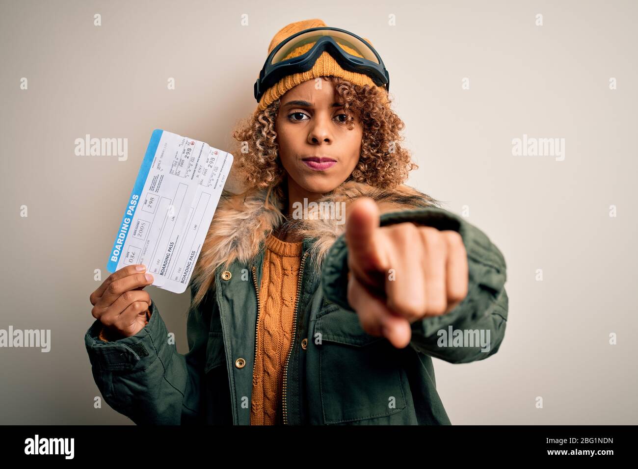 Joven turista afroamericana con gafas de esquí sosteniendo billetes de tarjeta de embarque de avión apuntando con el dedo a la cámara y a usted, señal de mano, Foto de stock