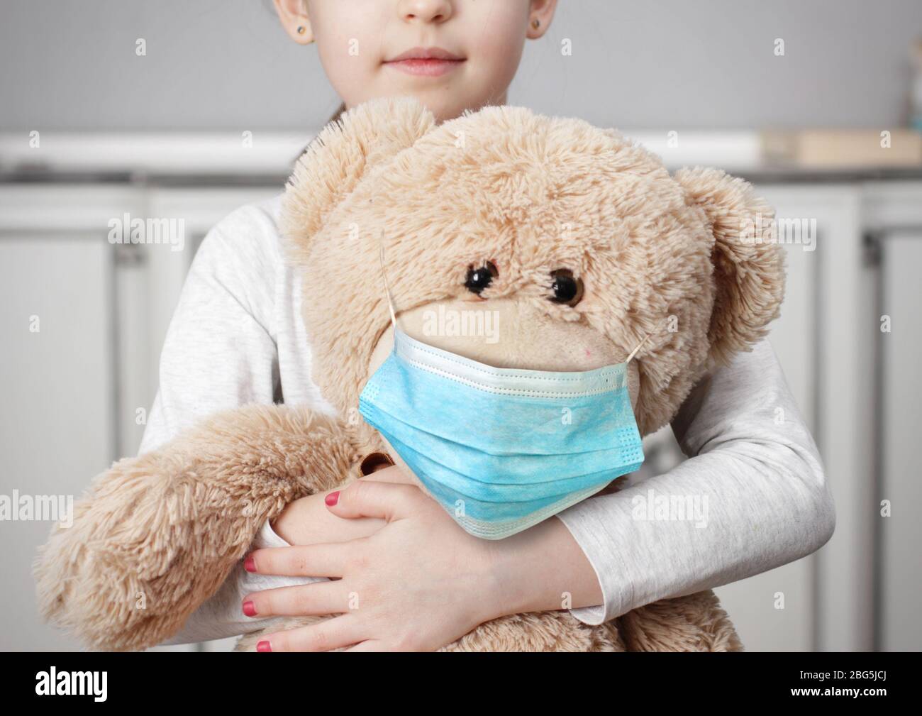 Niño en cuarentena debido a la epidemia de coronavirus. Niño niña acurruca juguete oso llevar máscara médica. Foto de stock