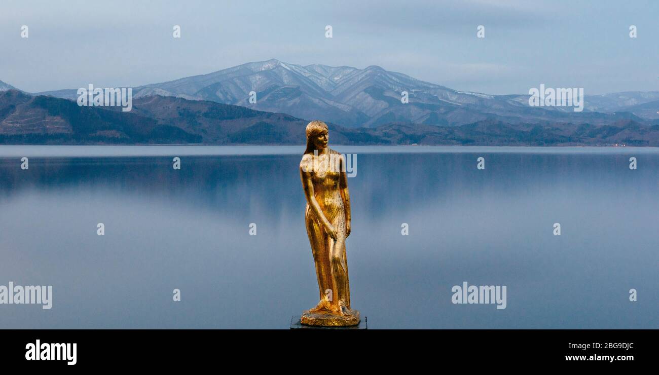 Una estatua de oro de Tatsuko se levanta contra las majestuosas aguas del lago Tazawa. Foto de stock