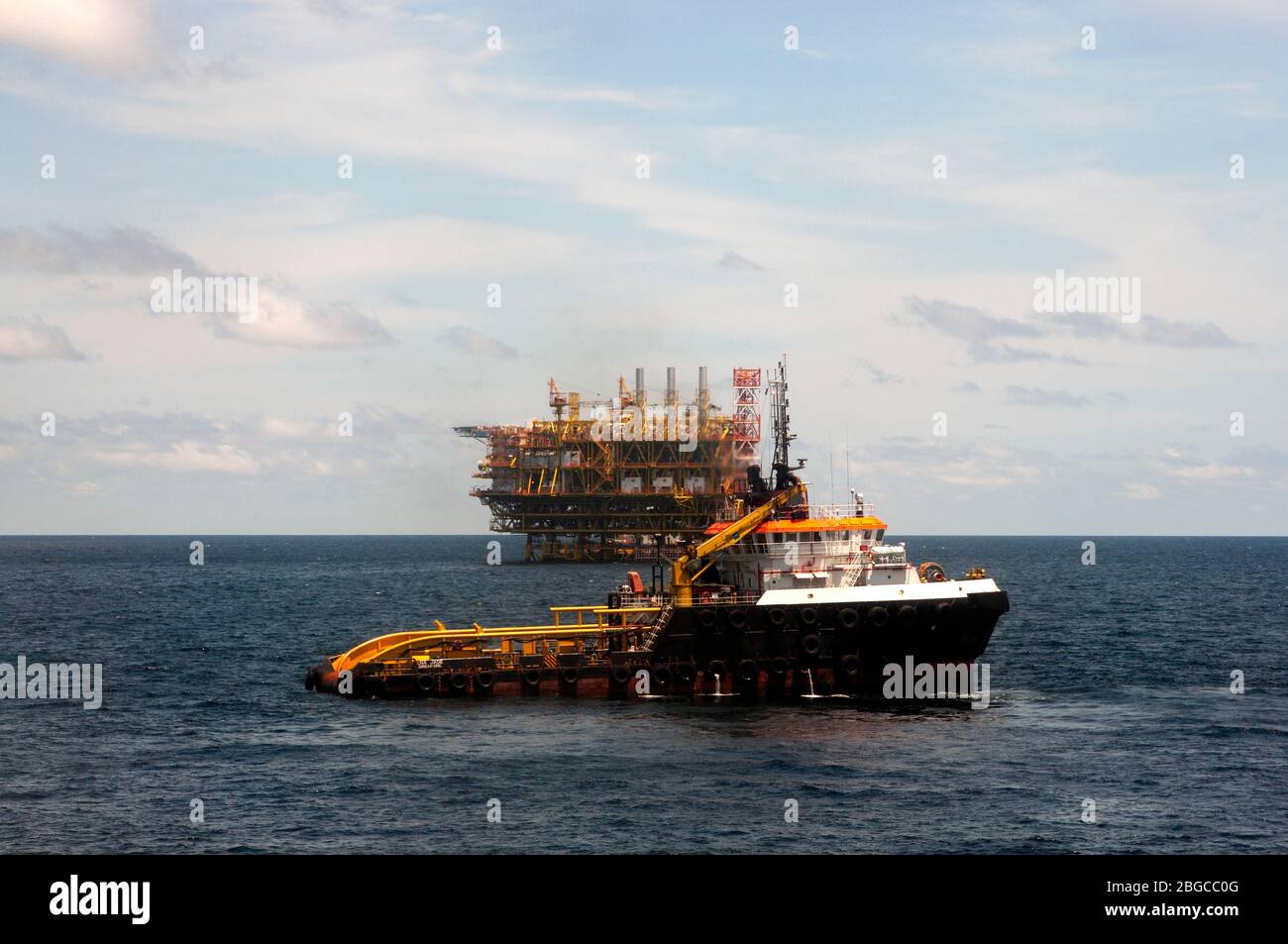 recipiente de suministro marino que vaporea alrededor de la plataforma petrolífera en el mar durante el día Foto de stock