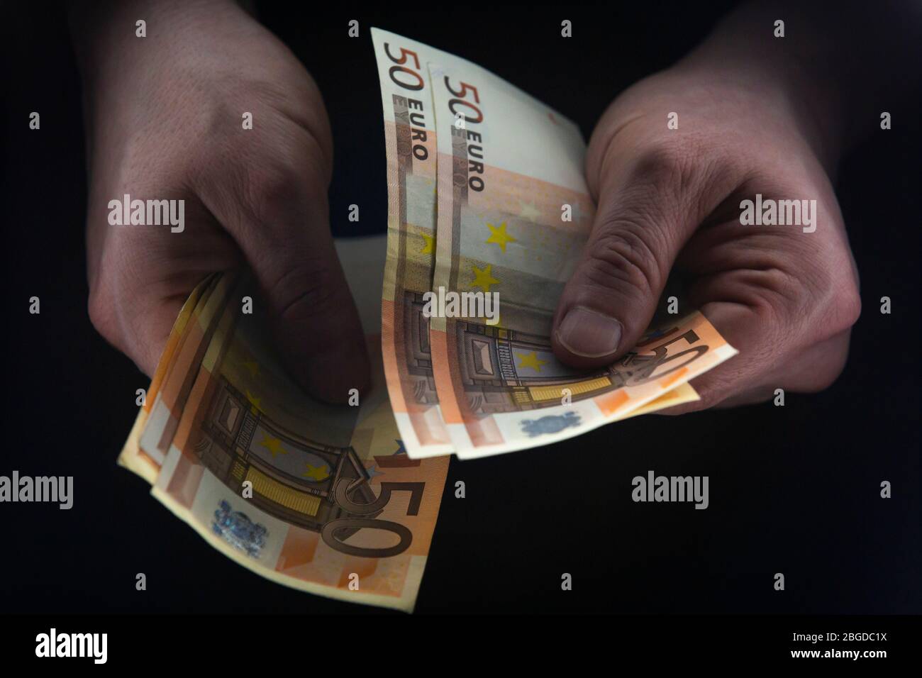 Hombre que sostiene 50 BILLETES DE EUROS en una habitación oscura, dinero ilegal, concepto de avaricia. Foto de stock