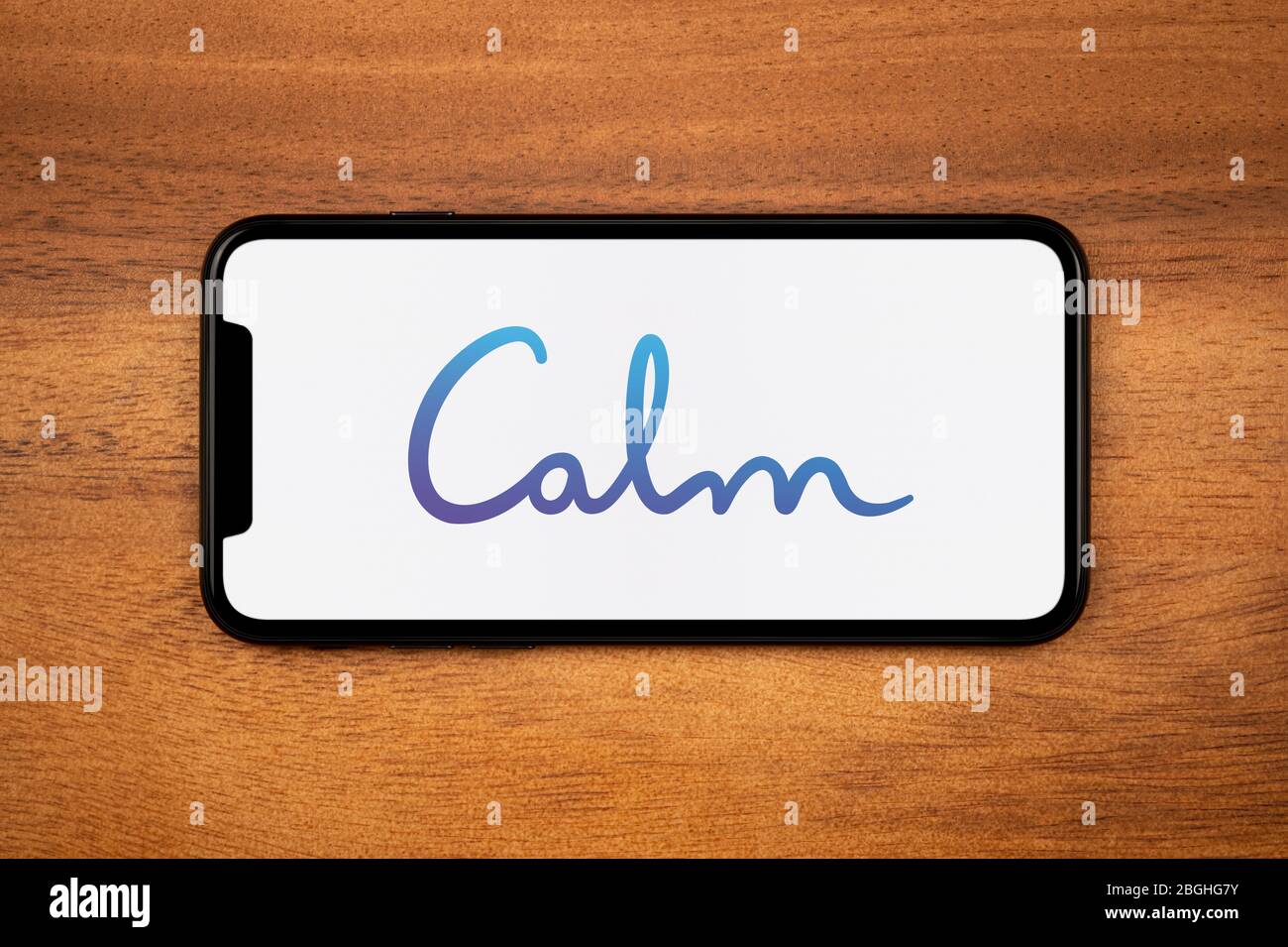 Un smartphone que muestra el logotipo de la aplicación Calm descansa sobre una mesa de madera plana (sólo para uso editorial). Foto de stock