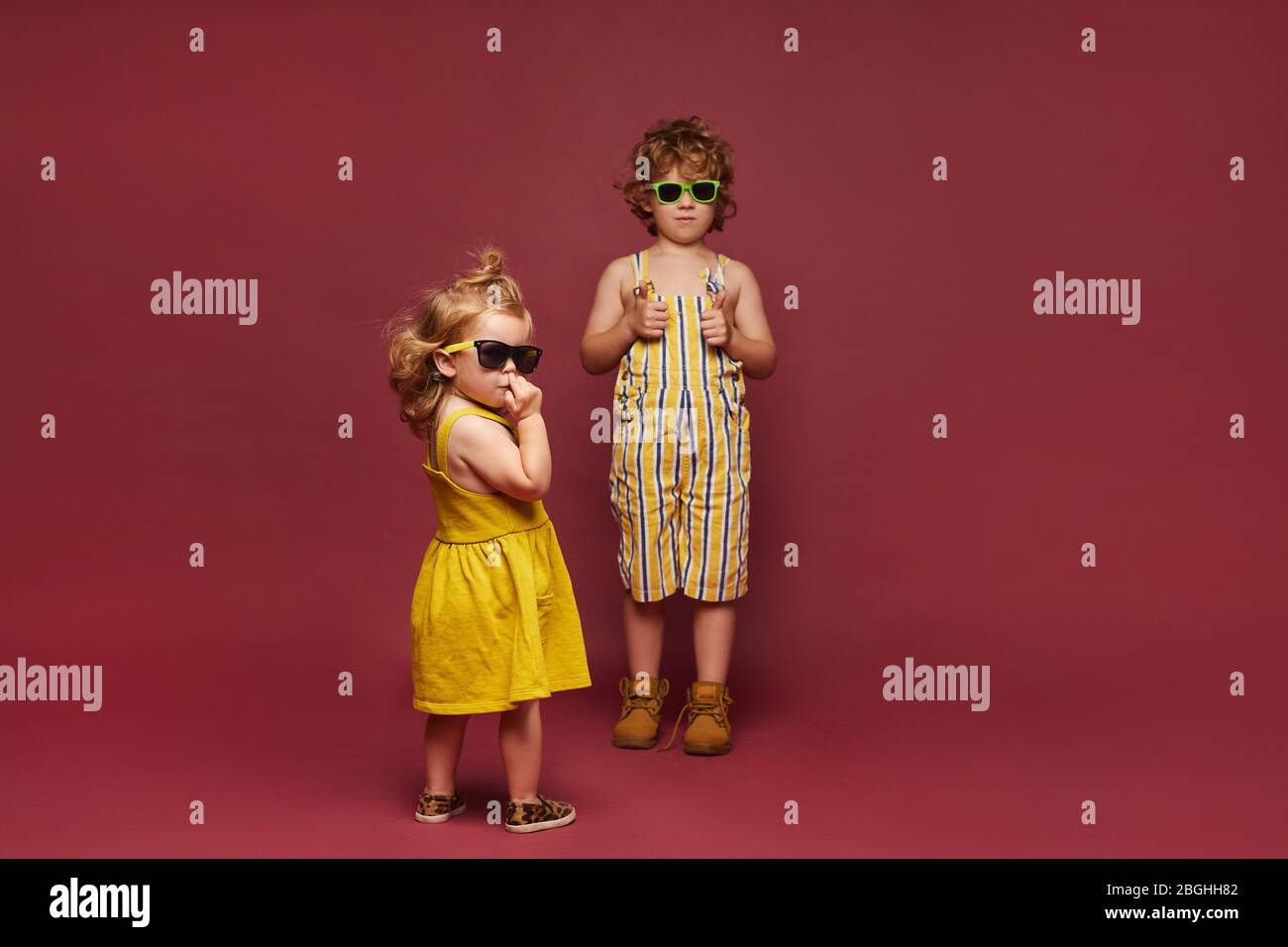 Niños con estilo y bonitos con ropa de moda posando sobre fondo rosa. Una  niña en un vestido y gafas de sol y un niño en un verano con estilo  overoles Fotografía