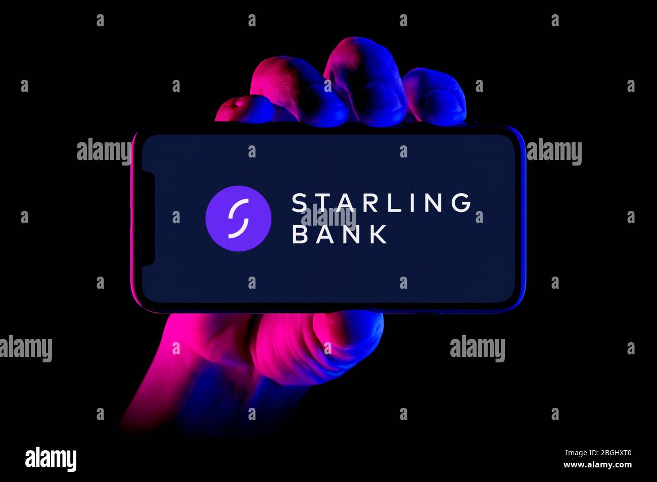 Un smartphone que muestra el logotipo de Starling Bank se mantiene con una toma manual sobre un fondo negro (sólo para uso editorial). Foto de stock