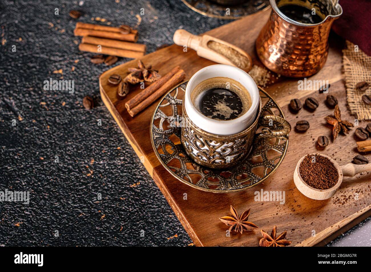 Taza de café turco sobre fondo negro con especias, granos de café y cafetera de arena Foto de stock