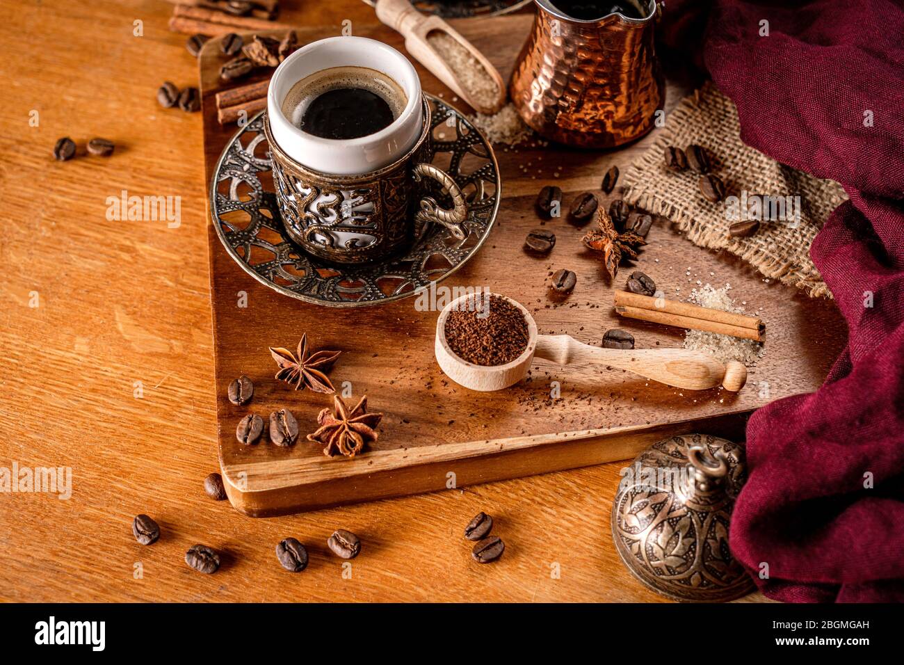 Detalle de una taza de café rodeada de granos de café y especias sobre un fondo de madera natural Foto de stock