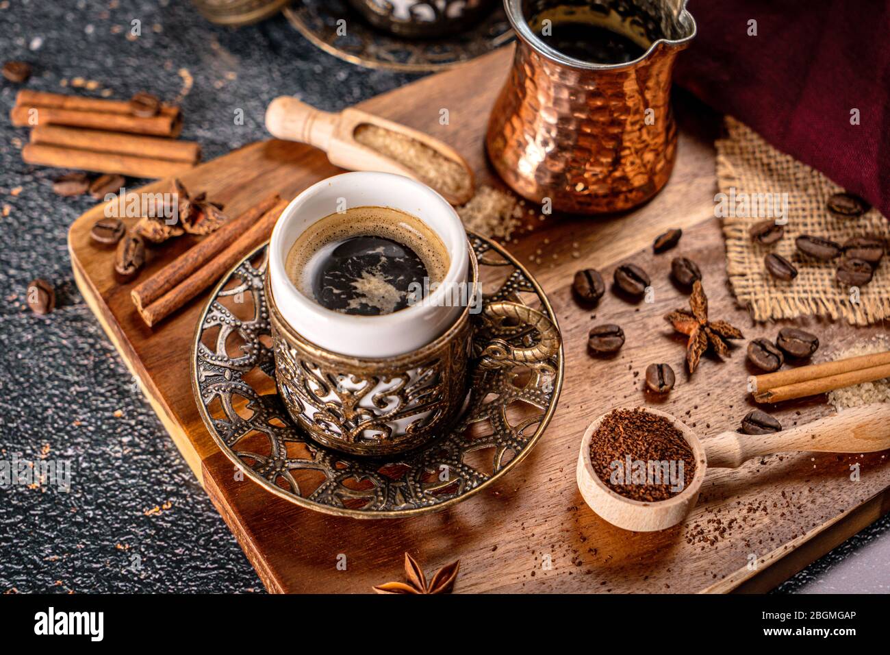 Taza de café turco sobre fondo negro con especias, granos de café y cafetera de arena Foto de stock