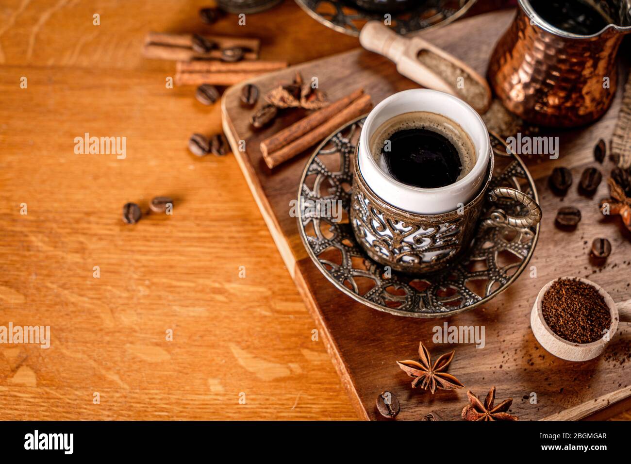 Detalle de una taza de café rodeada de granos de café y especias sobre un fondo de madera natural Foto de stock