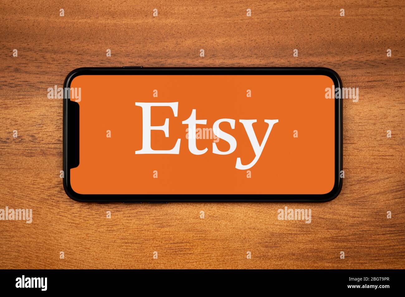 Un smartphone que muestra el logotipo de Etsy descansa sobre una mesa de madera plana (sólo para uso editorial). Foto de stock