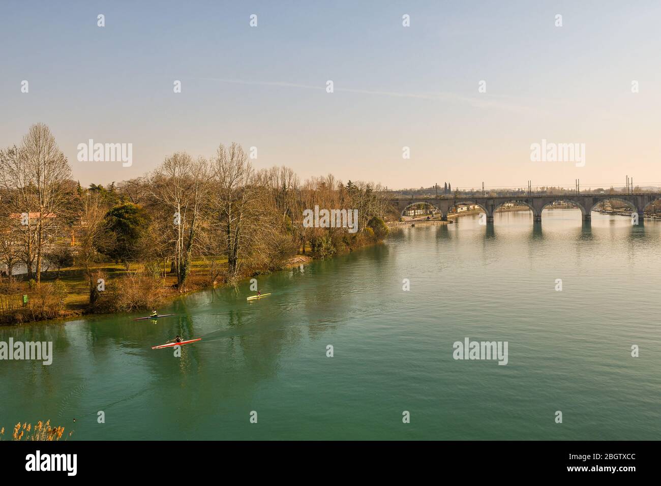 Vista elevada del río Mincio con tres hombres canotaje y el puente arqueado del ferrocarril en el fondo, Peschiera del Garda, Verona, Veneto, Italia Foto de stock