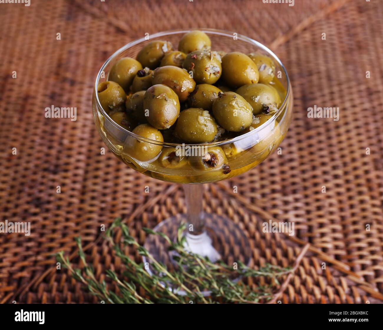 Aceitunas verdes en aceite con especias y romero en jarrón de cristal sobre la mesa Foto de stock