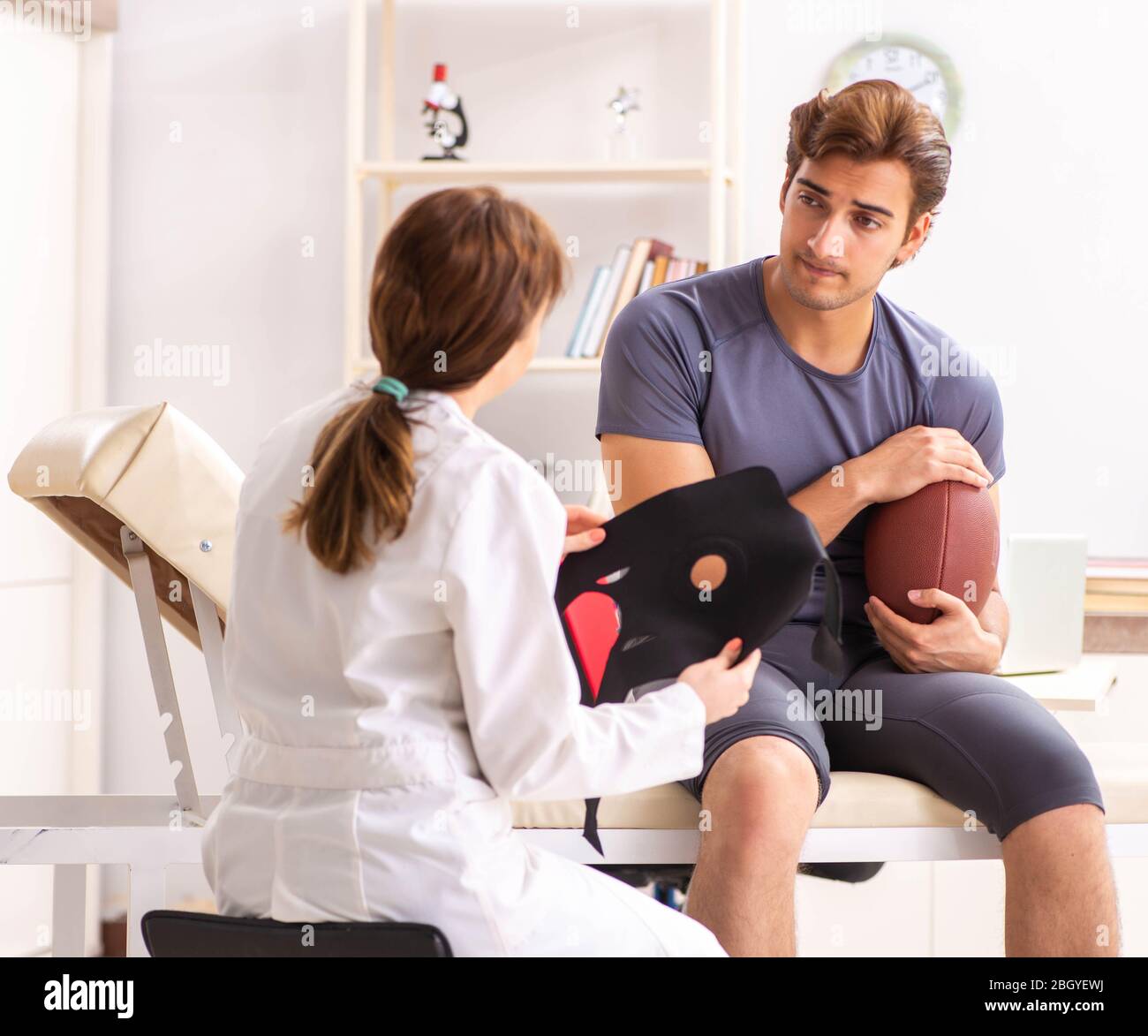 Guapo jugador de fútbol americano visitando doctora traumatologist Foto de stock