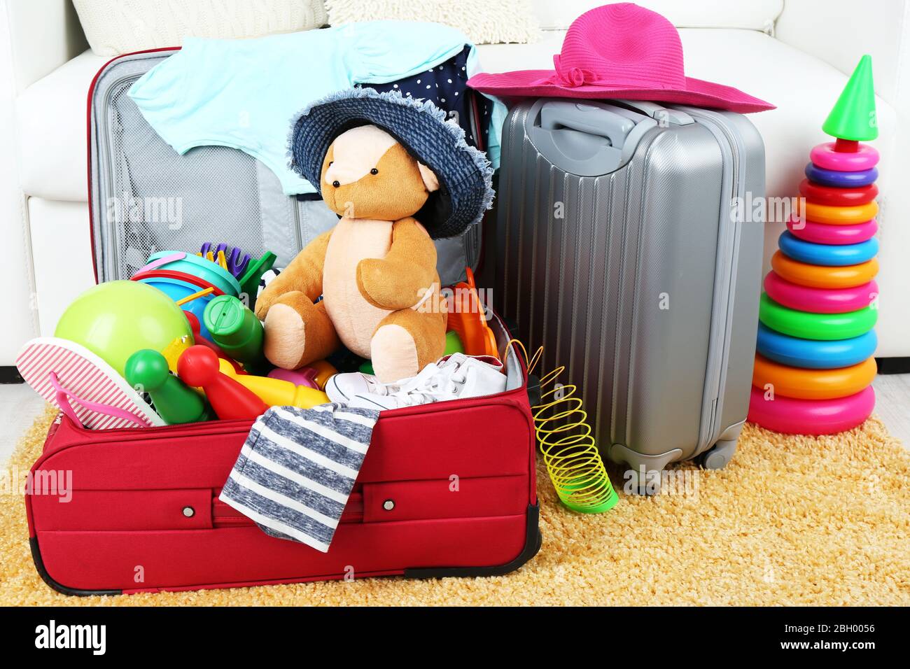 Maletas llenas de ropa y juguetes para niños sobre alfombra de piel y fondo  blanco de sofá Fotografía de stock - Alamy