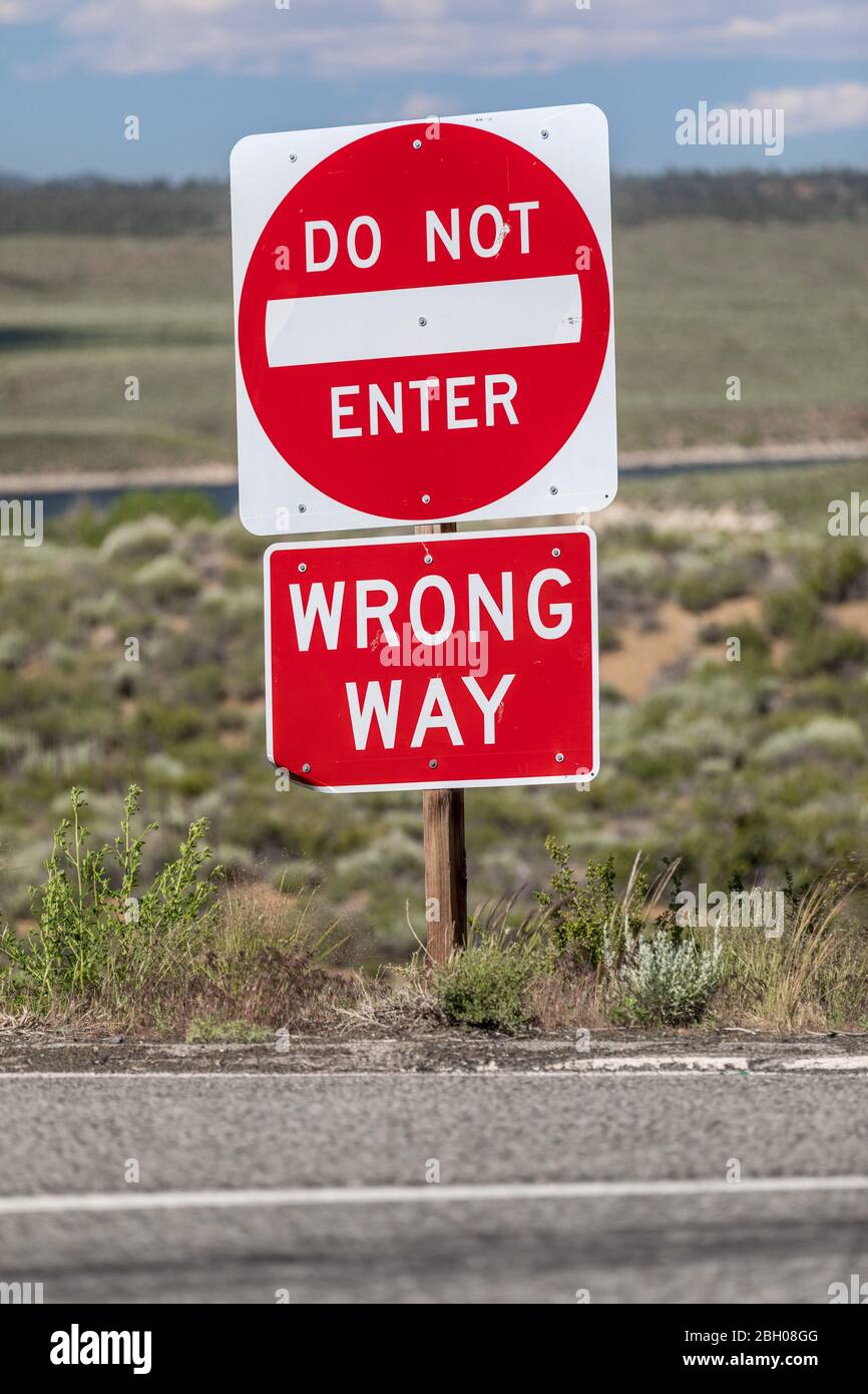 Primer plano de una señal roja de la calle al lado del cursor que dice "no entrar, camino equivocado" contra un paisaje rural solitario Foto de stock