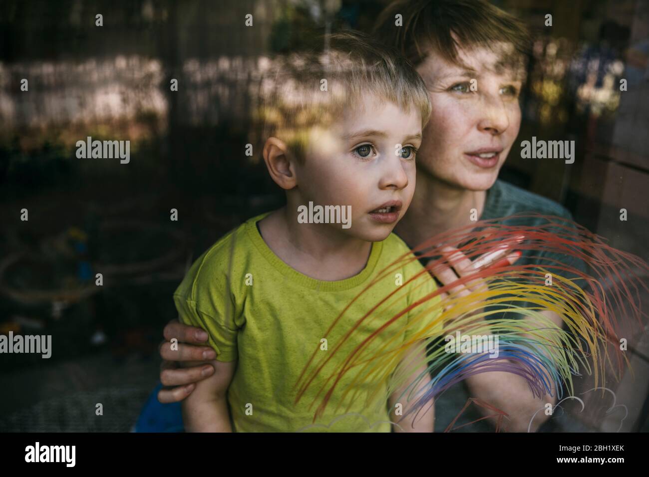Retrato de madre y su hijo pequeño mirando por la ventana con el arco iris dibujado Foto de stock
