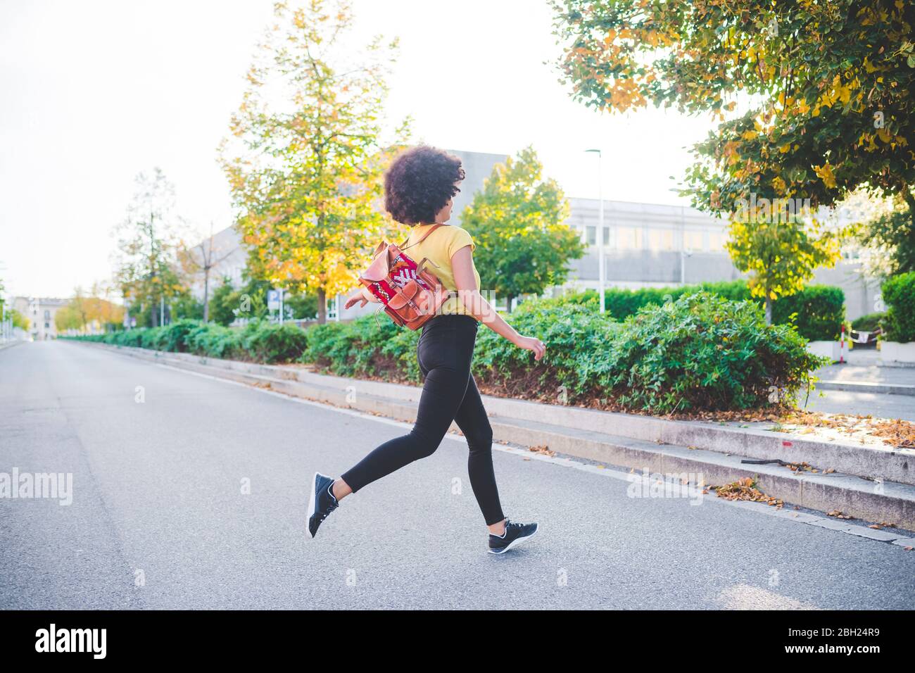 Mujer joven con un pelo de afro corriendo en una calle de la ciudad Foto de stock