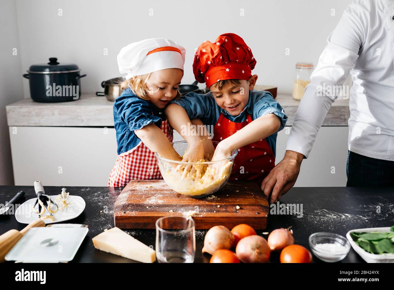 Los niños preparan la masa con el padre en la cocina en casa Foto de stock