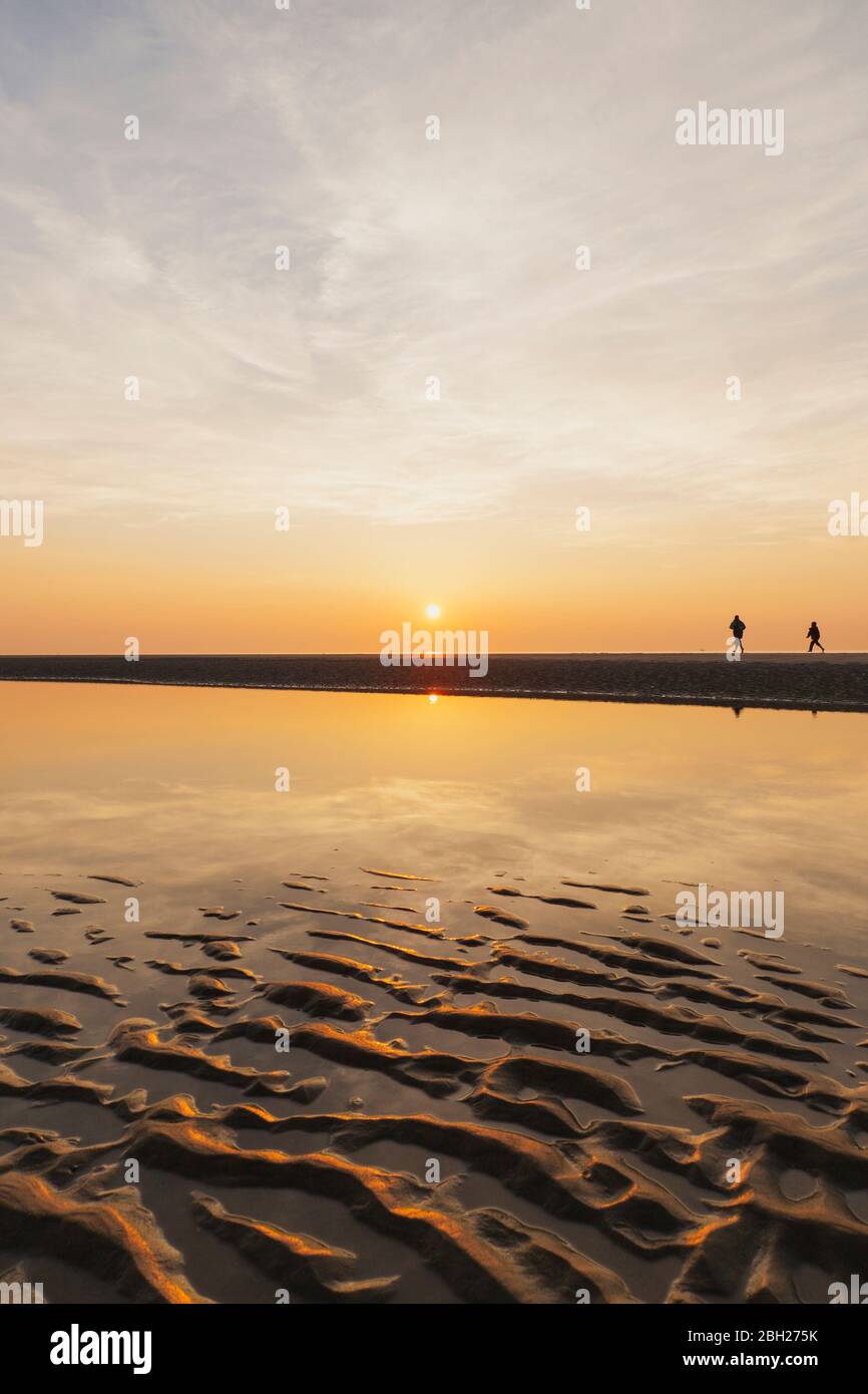 Vista distante de la silueta gente caminando en la playa contra el cielo durante la puesta de sol, Costa del Mar del Norte, Flandes, Bélgica Foto de stock