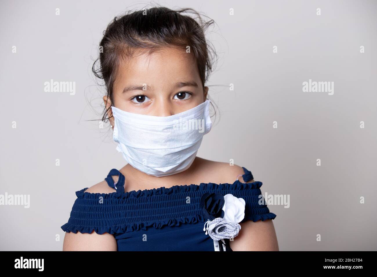Niña cara de niño cubierta con máscara en casa para prevenir la propagación de la infección del virus de la Corona. Foto de stock