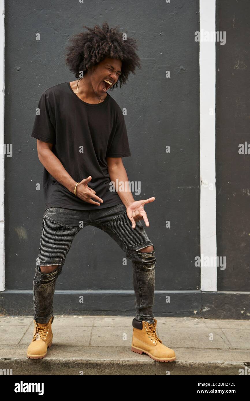 Joven negro con afro cantando y bailando frente a la pared gris Foto de stock