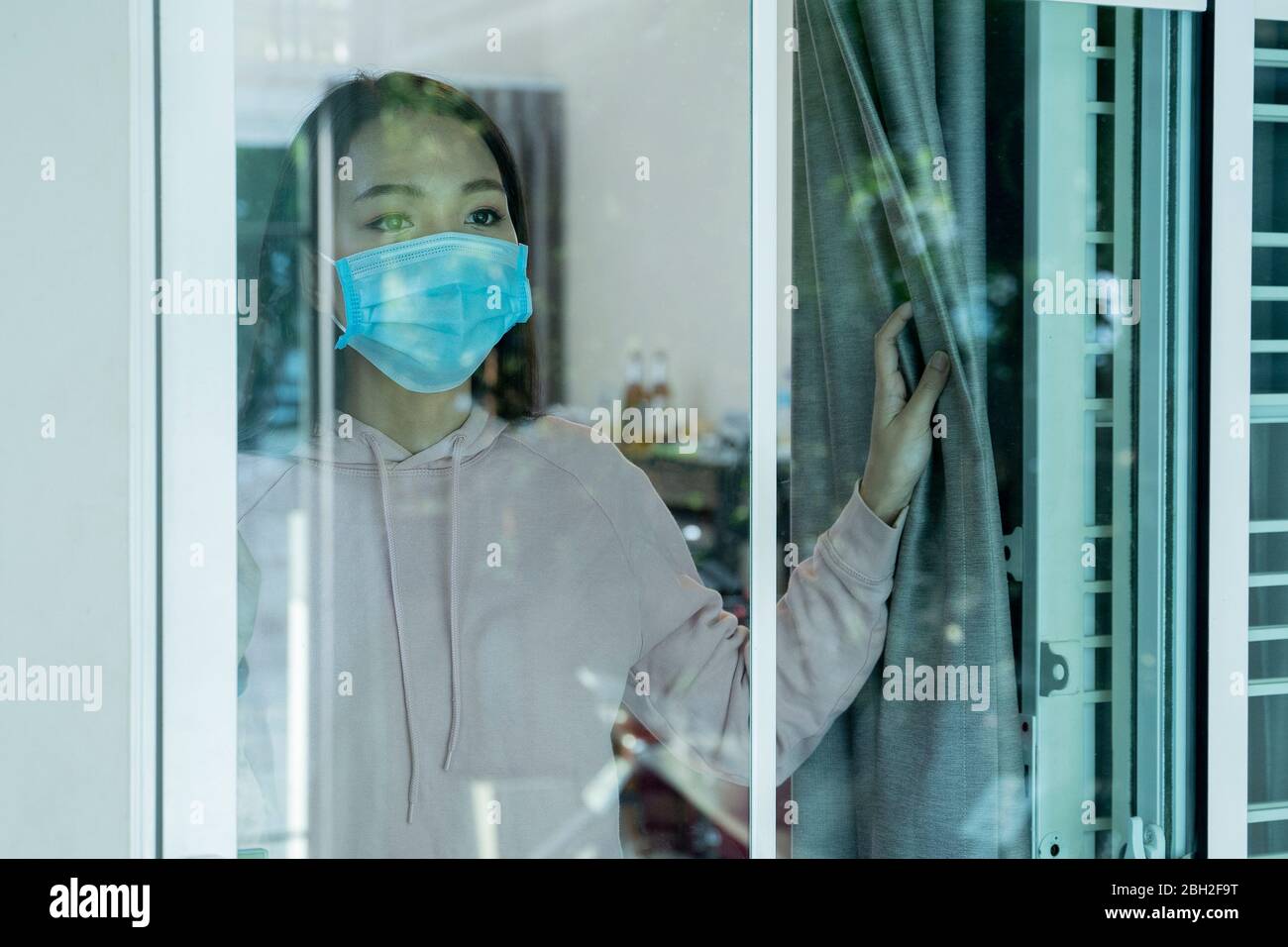Una mujer asiática con máscara mirando por la ventana. Foto de stock