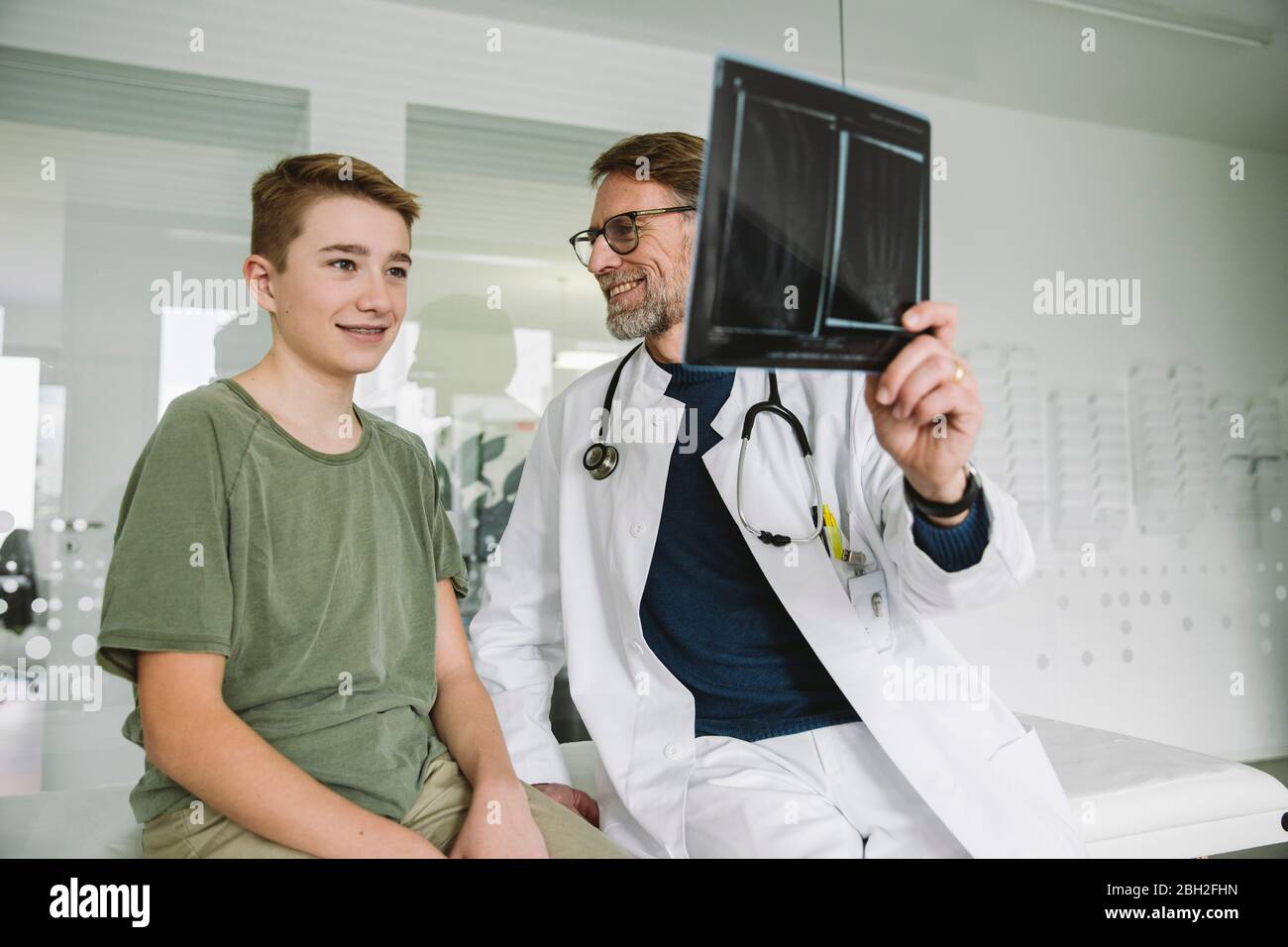 Médico explicando imagen de rayos X de mano rota a adolescente en la práctica médica Foto de stock