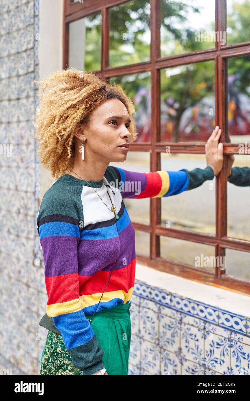 Retrato de una mujer joven con un estilo afro apoyado sobre una ventana de espejo Foto de stock