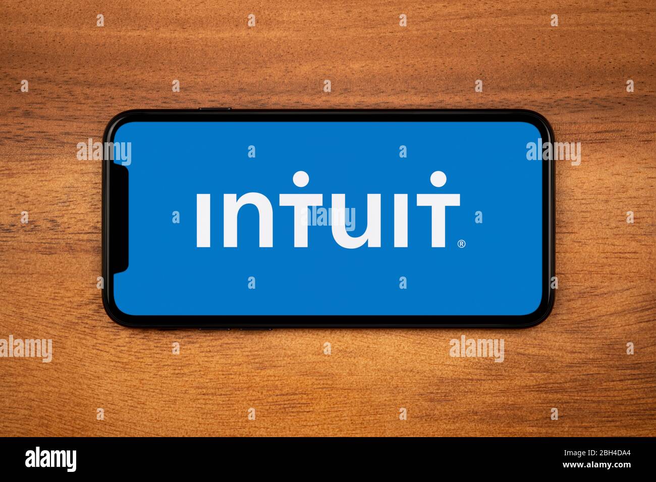 Un smartphone que muestra el logotipo Intuit descansa sobre una mesa de madera plana (sólo para uso editorial). Foto de stock