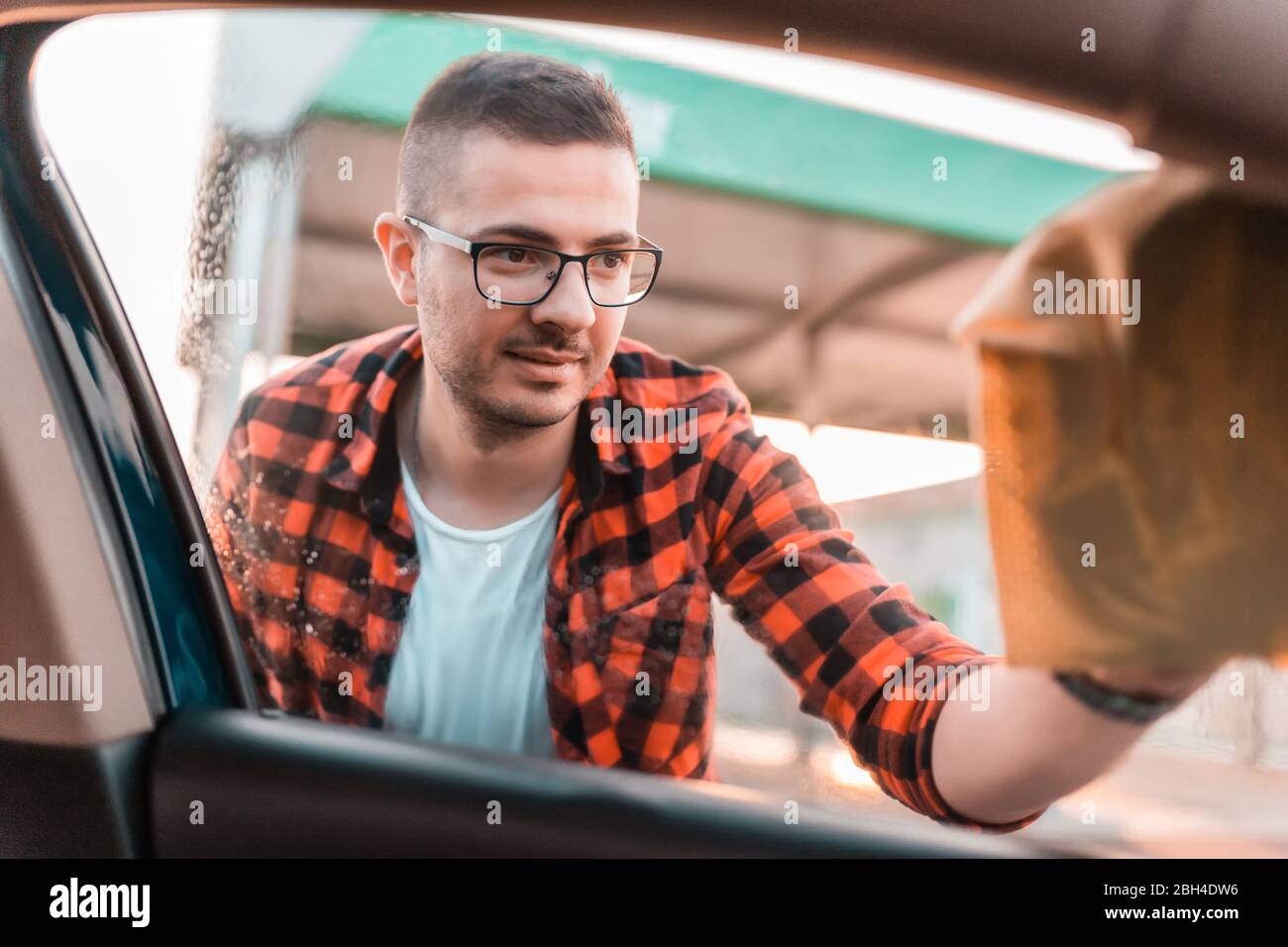 Disparo de un hombre joven limpiando las ventanas de su coche desde el exterior. Foto de stock