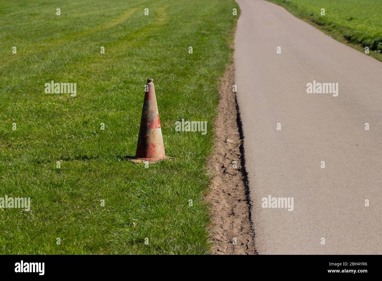 Cono de tráfico sucio y desgastado en la hierba al lado de una carretera Foto de stock