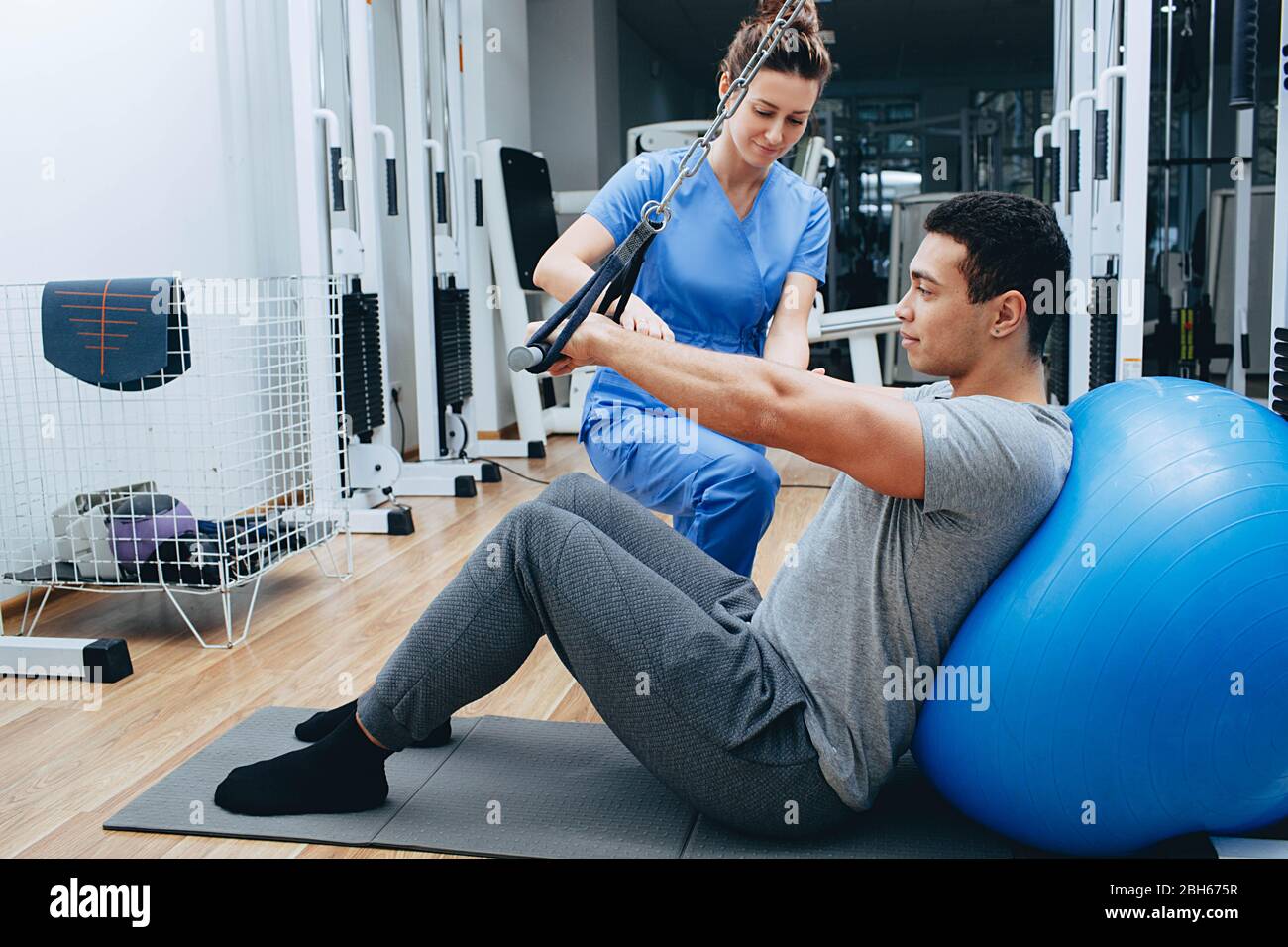 el kinesiólogo ayuda a un hombre de raza mixta a hacer ejercicios para fortalecer sus músculos de la espalda. tratamiento del dolor de espalda mediante kinesioterapia. Foto de stock