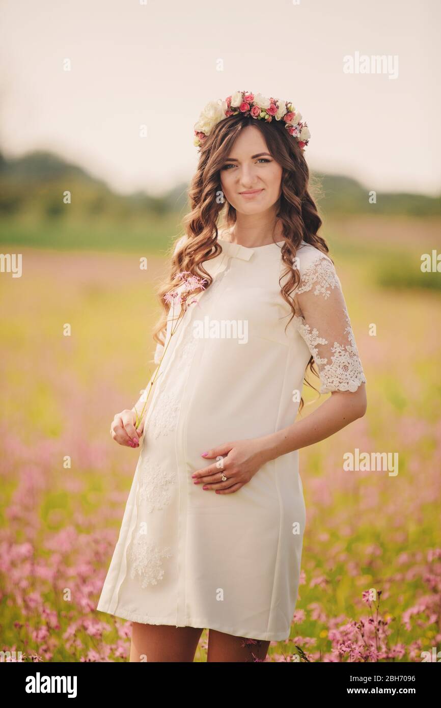 Retrato de una mujer embarazada en fieida de flores rosadas. Joven hermosa niña embarazada con una corona de flores en la cabeza en el sol. Maternidad. SPRI Fotografía de stock - Alamy Retrato de una mujer embarazada en fieida de flores rosadas. Joven hermosa niña embarazada con una corona de flores en la cabeza en el sol. Maternidad. SPRI Fotografía de stock - Alamy