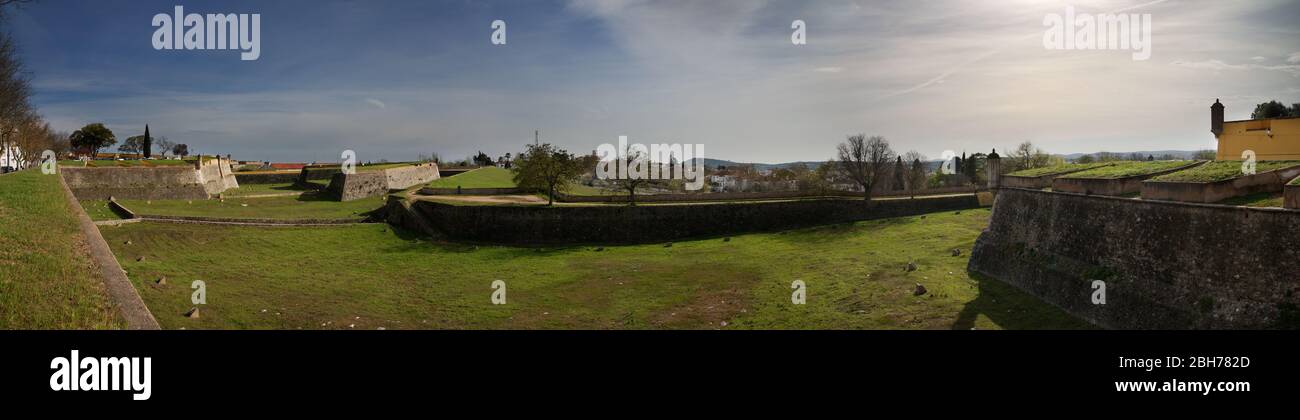 Amplio panorama del foso entre las paredes defensivas interiores y exteriores de la ciudad fronteriza de Garrison Elvas bajo un cielo azul nublado. Alentejo, Portugal. Foto de stock