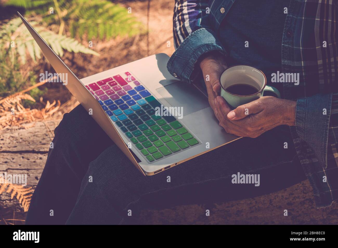 mujer cercana al aire libre con taza de café y un portátil en las piernas listo para trabajar y utilizar la conexión a internet - trabajando en todas partes sin límite de edad para la gente moderna y gratuita con ordenador y señal wifi Foto de stock