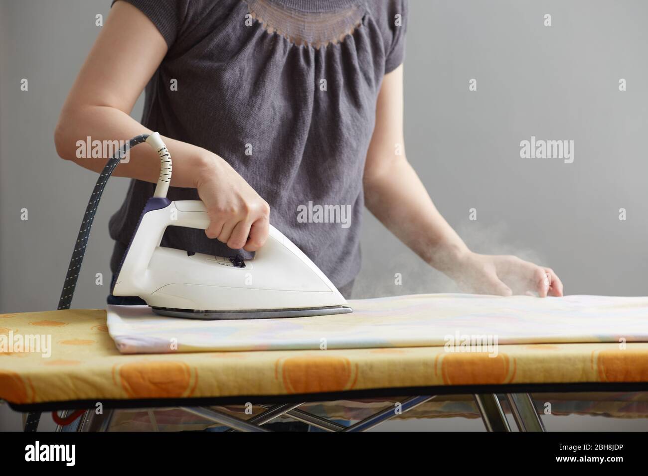 las manos femeninas sostienen una plancha blanca y una plancha sobre una tabla planchar. Primer plano. Sin rostro. Copiar espacio sobre fondo gris. Deberes del hogar y cuidado del