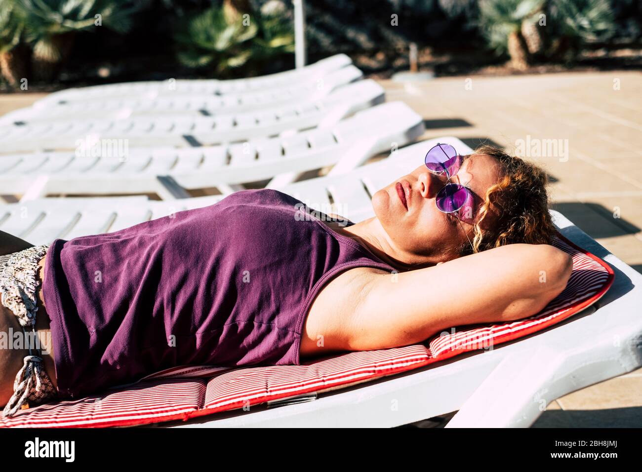Hermosa mujer caucásica de edad media lat abajo haciendo el sol en verano en las tumbonas. Relajado y dormir bajo el sol - vacaciones concepto - colores violetas Foto de stock