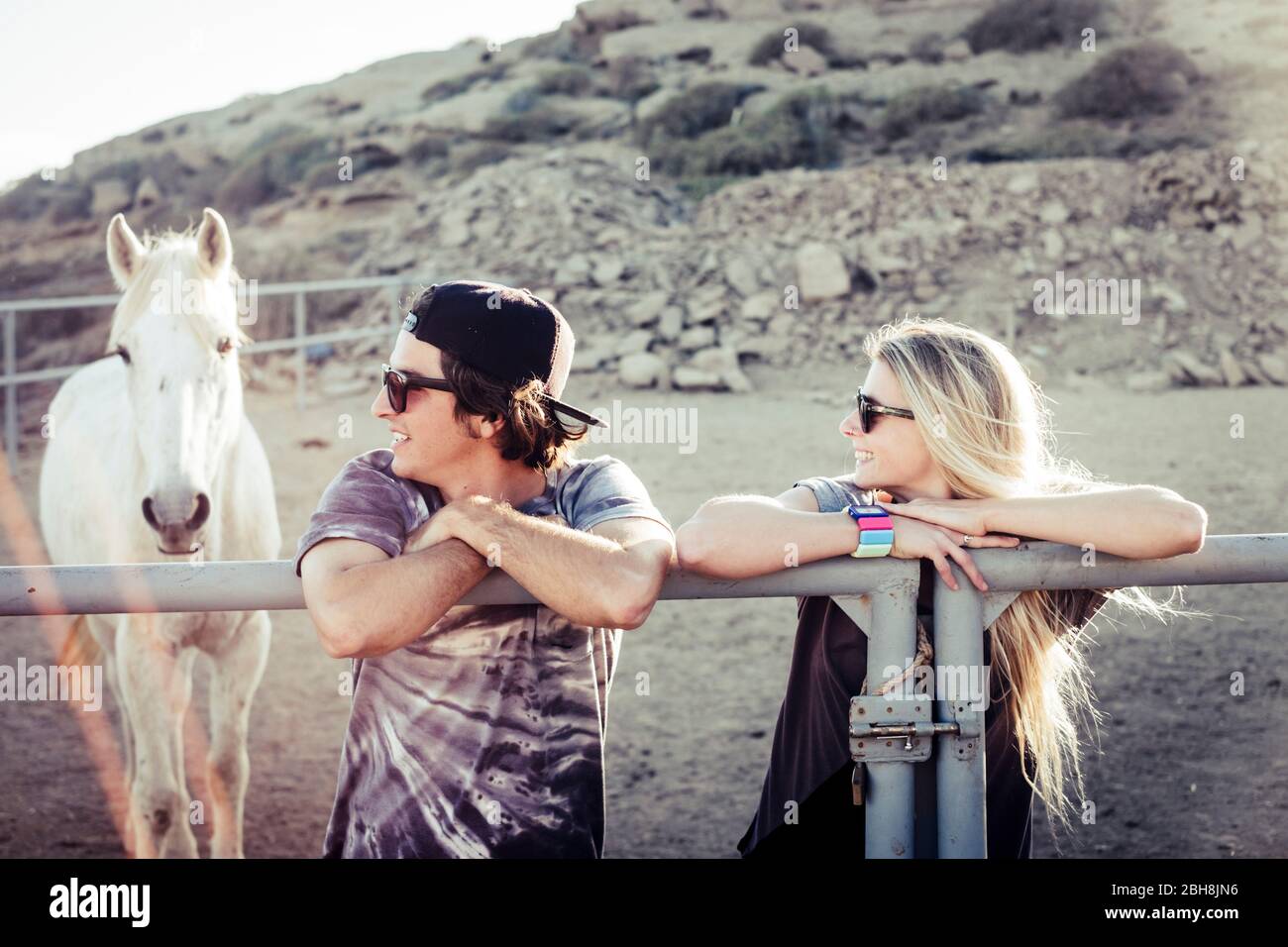 Pareja de jóvenes caucásicos niño y niña dentro de la caja de caballo con blanco hermoso animal en el fondo - la amistad y disfrutar de la naturaleza al aire libre concepto Foto de stock